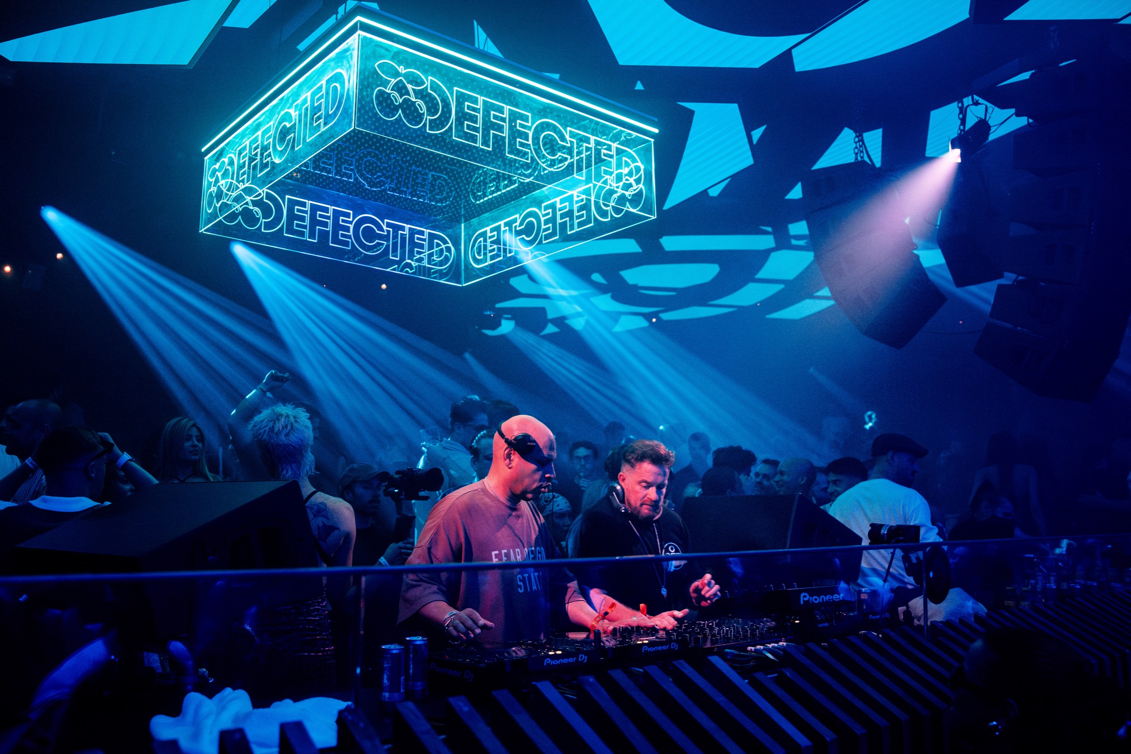 DJs performing behind Pioneer decks with Defected neon sign at Pacha Ibiza
