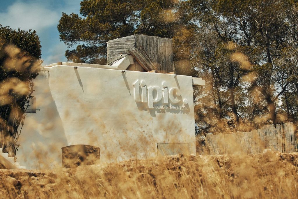 Tipic Club Formentera white building exterior surrounded by golden grass fields